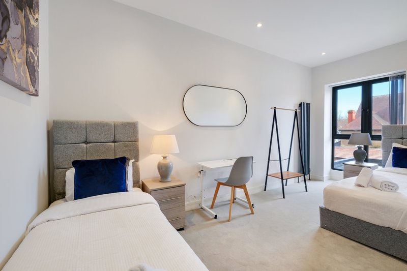 Modern bedroom with twin beds, grey upholstered headboards, desk area and city view through large windows