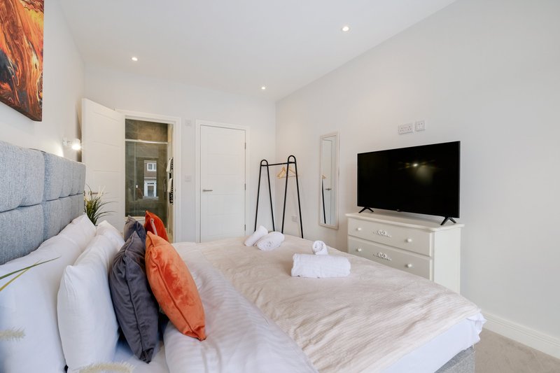 Modern bedroom with double bed, white bedding, orange cushions, TV on dresser, and ensuite bathroom door