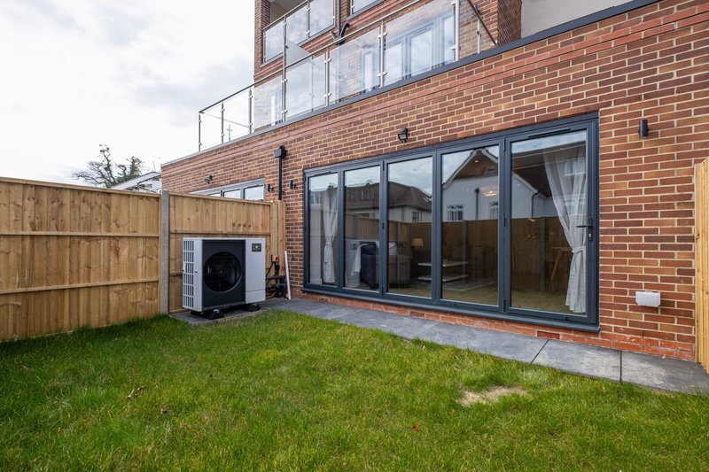Brick residential building exterior with garden, wooden fence, and large glass doors