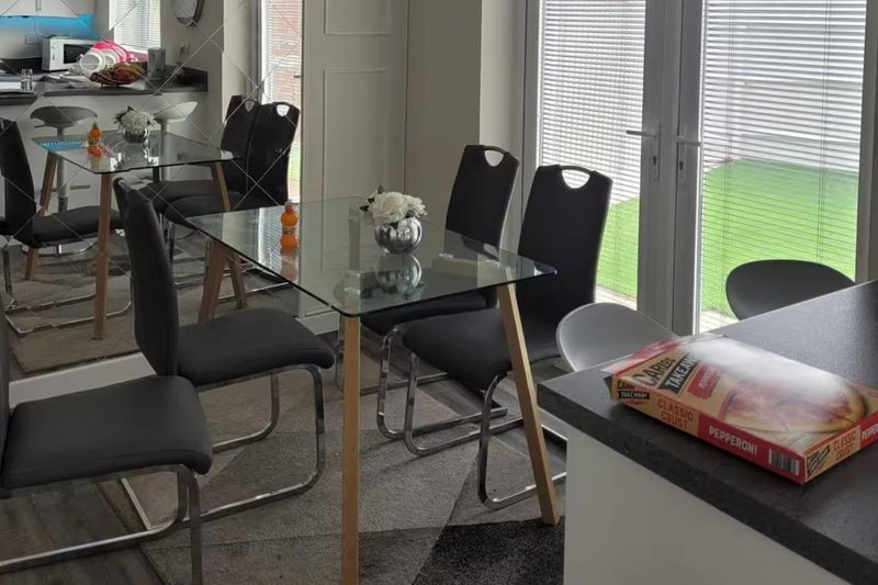 Modern dining area with glass table, black chairs, and views to garden through patio doors