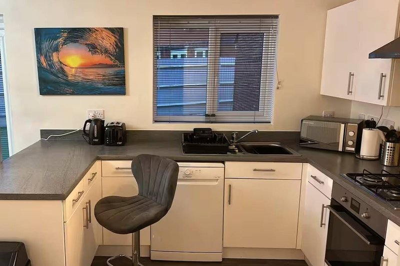 Kitchen with cream cabinetry, dark countertop, gas cooker, and small dining chair