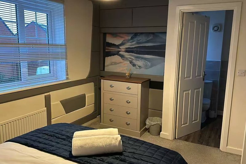 Bedroom with double bed, wooden drawers, framed landscape artwork, and white door to ensuite