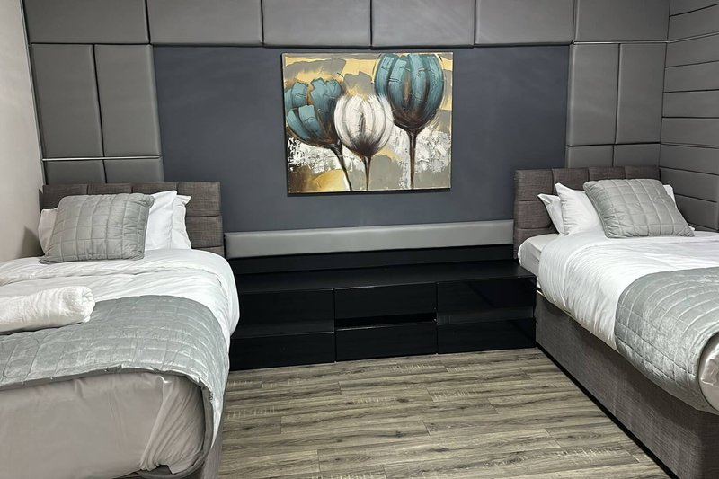 Twin bedroom with two single beds, grey bedding, wooden flooring and wall art