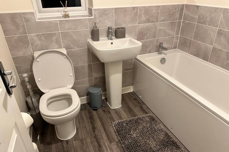 Modern bathroom with toilet, pedestal sink, bathtub, and tiled walls