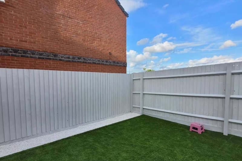 Outdoor garden area with artificial grass, metal fencing, and brick building wall