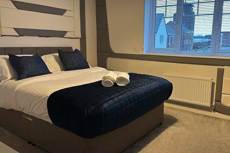 Modern bedroom with double bed, navy bedding, white pillows and city view from window