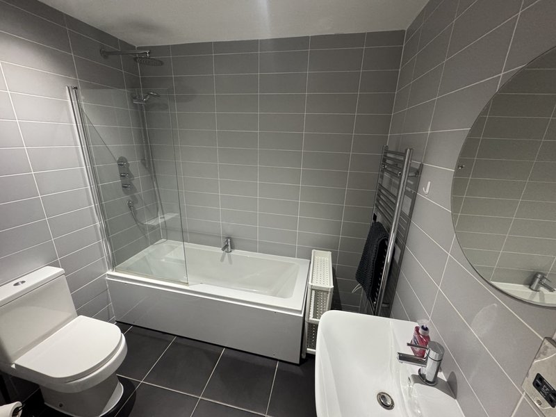 Modern bathroom with grey tiles, white bath with shower screen, toilet and sink