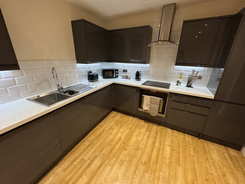 Modern kitchen with dark cabinetry, white subway tile backsplash, stainless steel appliances and wooden flooring