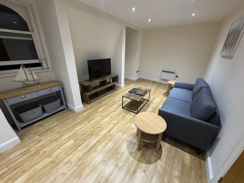 Open-plan living room with blue sofa, wooden flooring, TV on stand, and coffee table