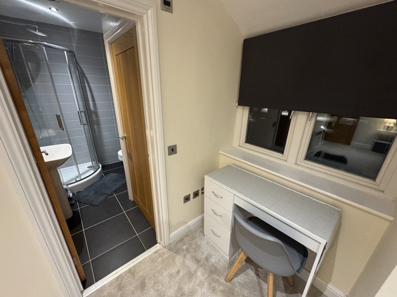 Bedroom with desk, chair, and en-suite bathroom visible through open door