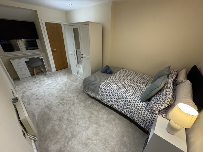 Spacious bedroom with double bed, wardrobe, desk area, and gray carpet flooring