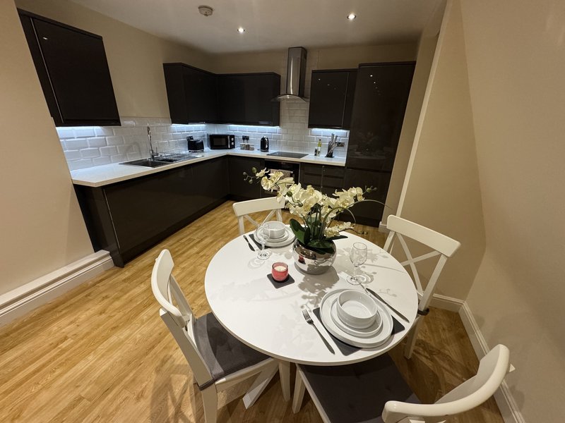 Modern kitchen and dining area with black cabinetry, white tile backsplash, round white dining table with place settings and white flowers