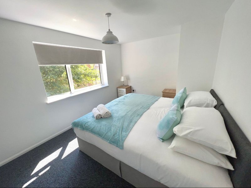 Bright bedroom with double bed, turquoise bedding, pendant lamp and window with blinds