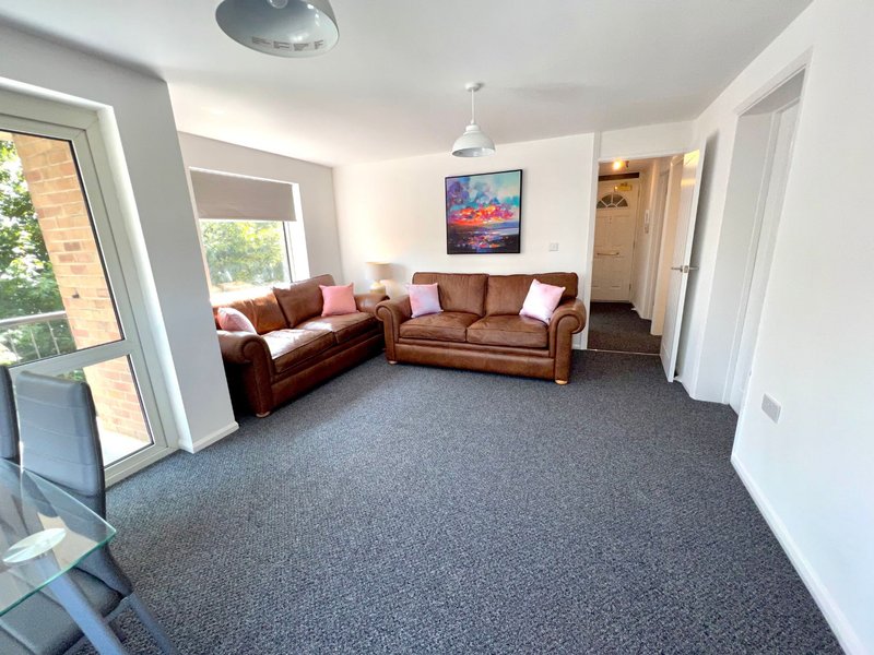 Spacious living room with brown leather corner sofa, gray carpet, wall art, and glass doors to garden