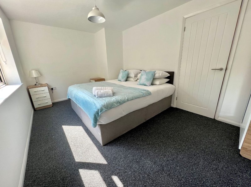 Bright bedroom with double bed, blue bedding, dark carpet, white wardrobe and pendant light