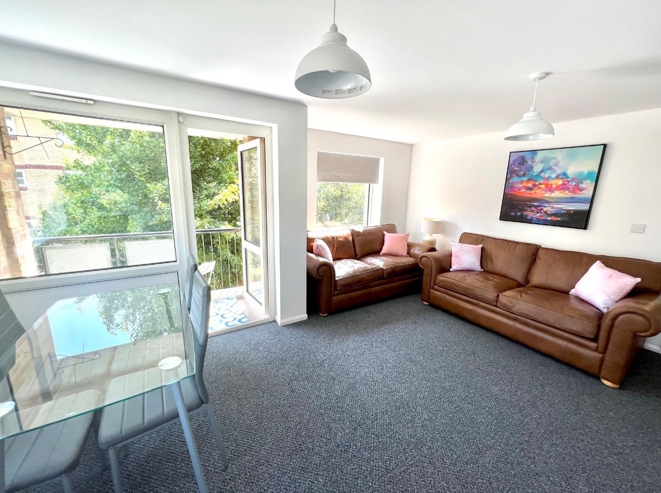 Bright living room with brown leather sofas, pendant lighting, wall-mounted TV and patio doors overlooking garden