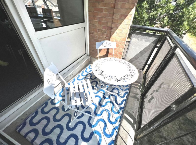 Small outdoor patio area with blue and white patterned rug, white table, chairs and brick wall