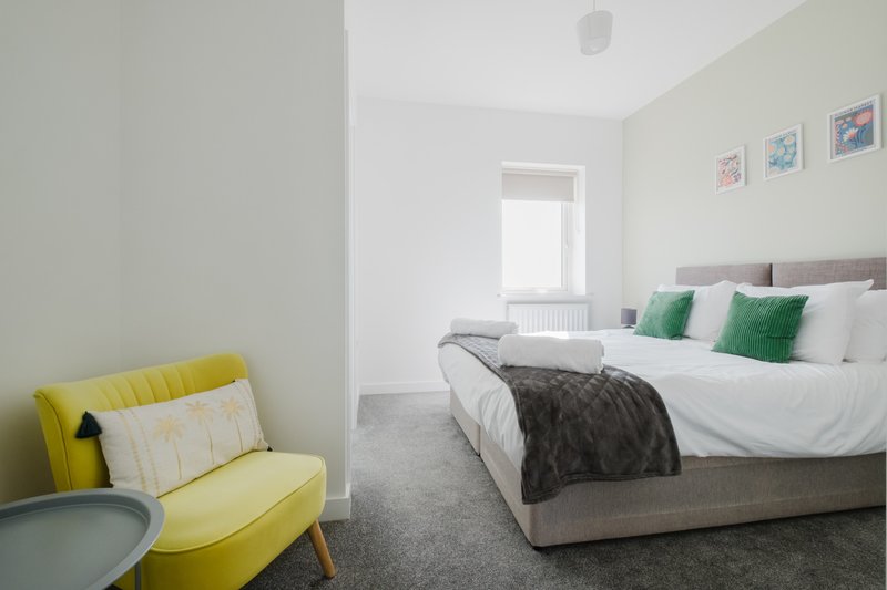 Bright modern bedroom with double bed, yellow armchair, and framed wall art