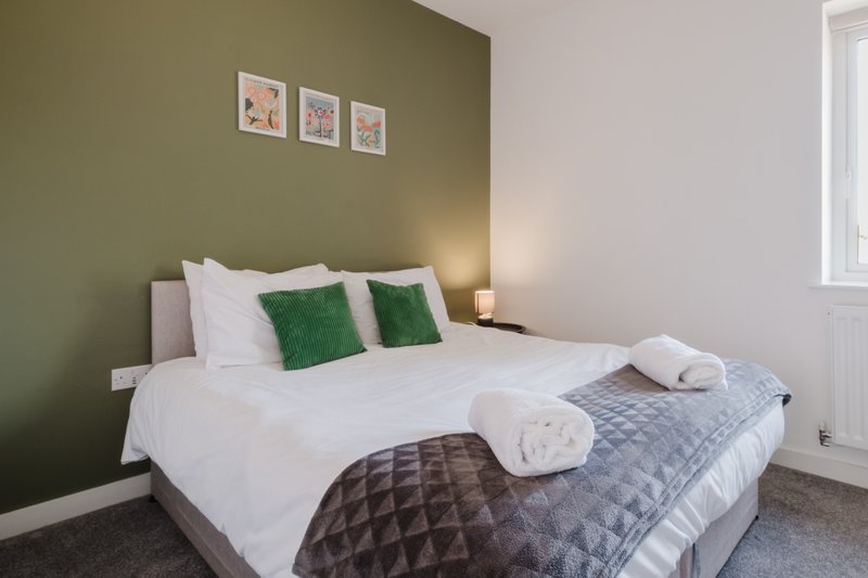 Bedroom with double bed, white linens, green accent pillows, olive wall and framed artwork