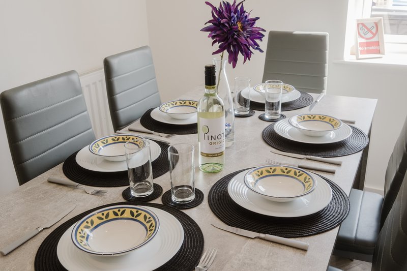 Formal dining table set with place settings, wine bottle, purple flowers and grey upholstered chairs
