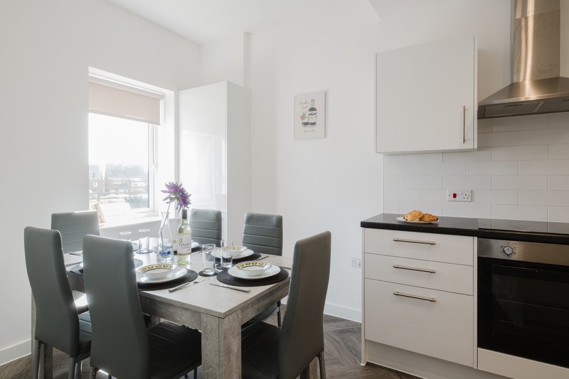 Modern kitchen-diner with white cabinetry, dining table, grey chairs and city view window