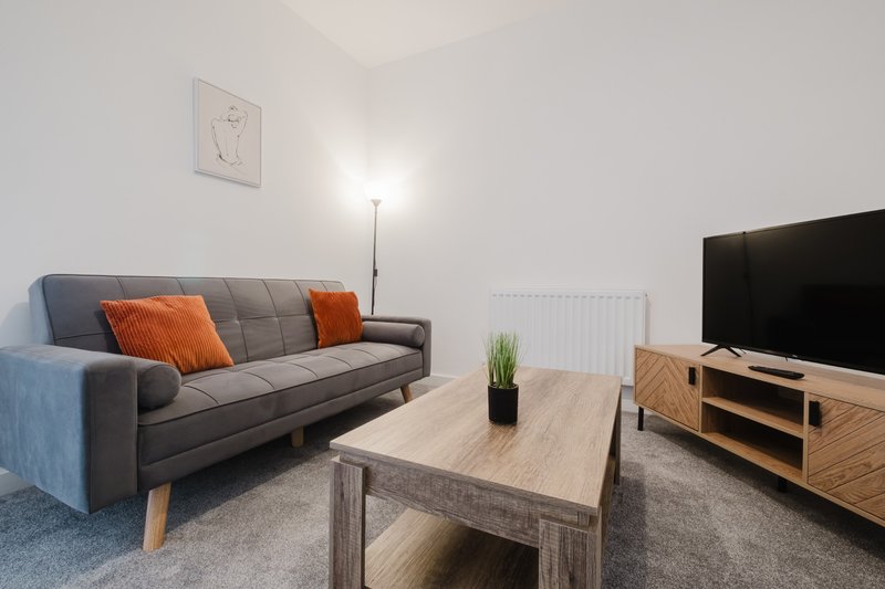 Living room with gray sofa, orange cushions, wooden coffee table and TV unit