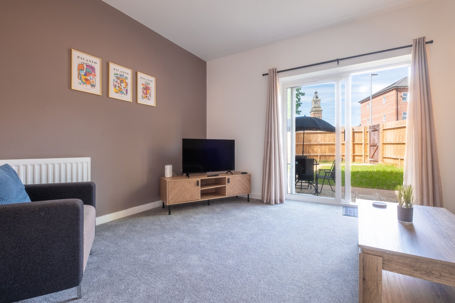 Modern living room with grey carpet, TV unit, armchair, and patio doors overlooking garden