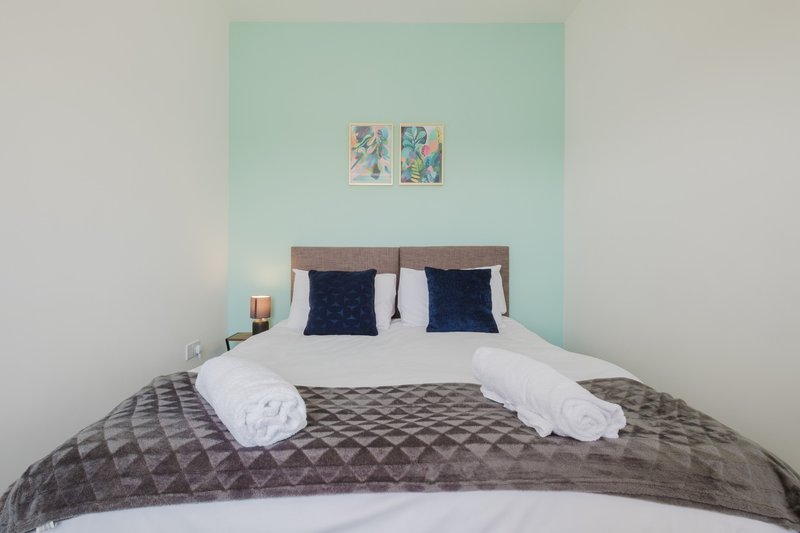 Bedroom with double bed, gray quilted bedding, navy cushions, and mint green accent wall