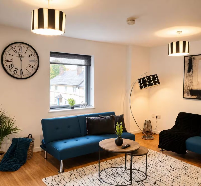 Modern living room with blue sofa, wooden floor, wall clock, and pendant lighting