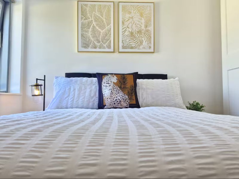 Bright bedroom with double bed, patterned bedding, decorative cushions and botanical wall art