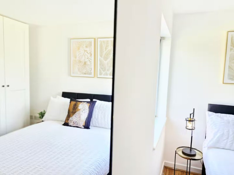 Bright bedroom with double bed, black headboard, decorative pillows and framed botanical prints