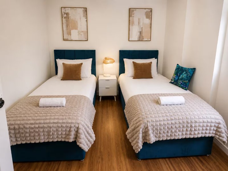 Twin bedroom with two single beds, navy headboards, white pillows, gold cushions, wooden floor