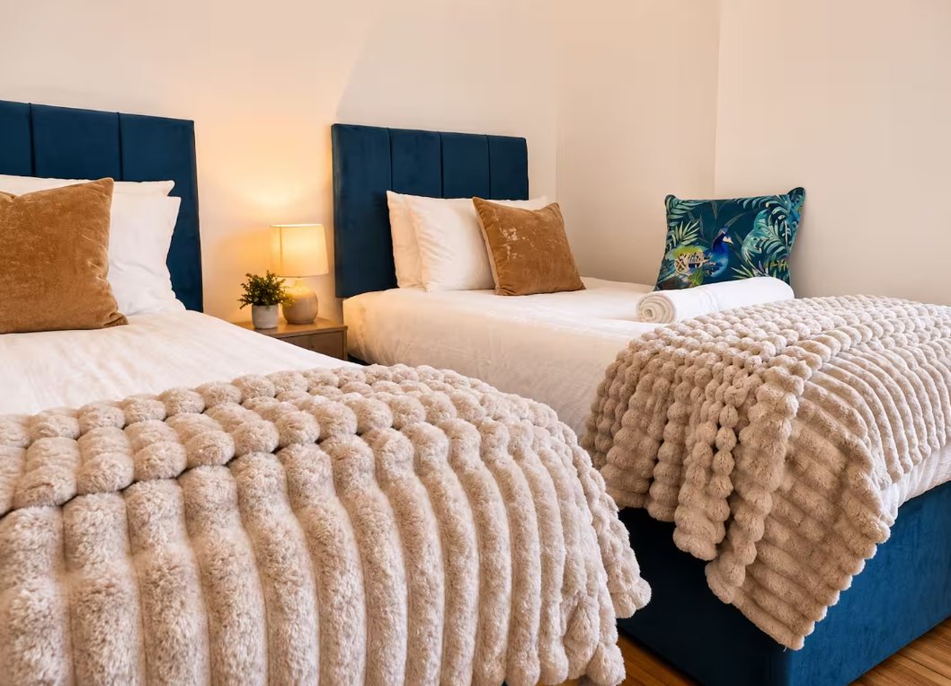 Twin bedroom with two double beds, navy headboards, textured beige bedding and decorative pillows