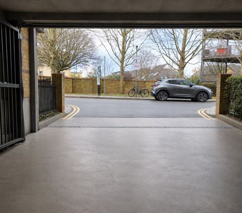 Modern driveway with open gates, parked car, and tree-lined street beyond