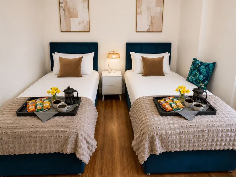 Twin bedroom with two single beds, navy headboards, white bedding, wooden floor and breakfast trays