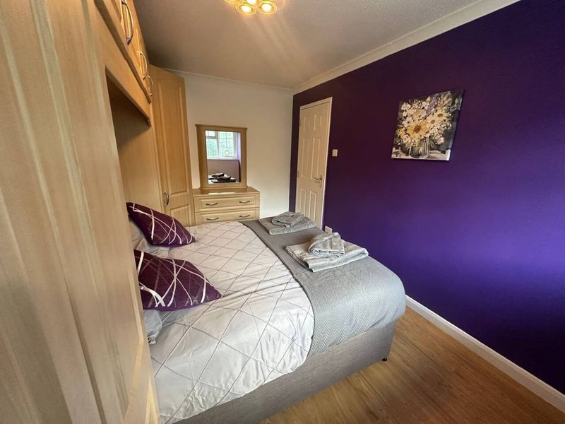 Bedroom with double bed, purple accent wall, wooden wardrobe and hardwood flooring
