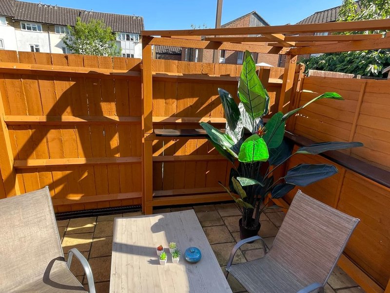 Enclosed wooden patio with pergola, potted plant, lounge chairs and table
