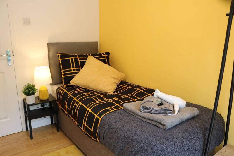 Bedroom with single bed, yellow accent wall, black bedside table and lamp