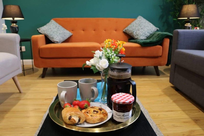 Living room with orange sofa, grey chairs, coffee table with flowers and refreshments