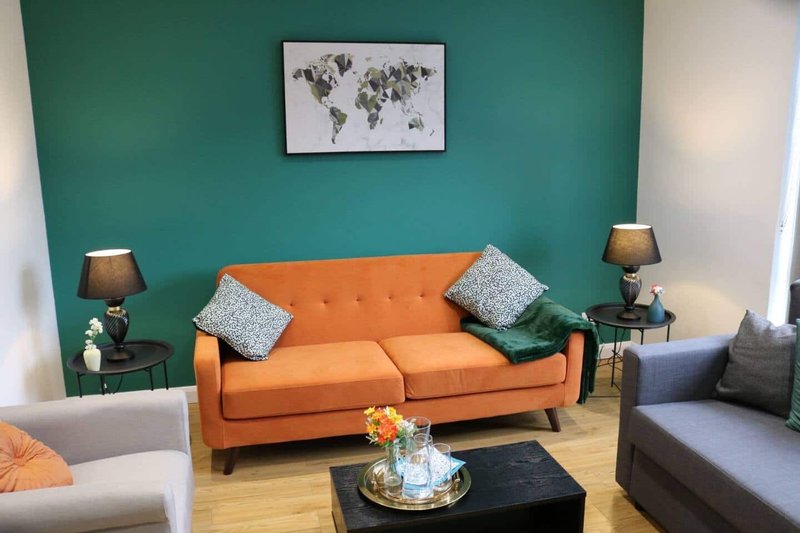 Living room with orange sofa, teal accent wall, world map art, and side tables with lamps