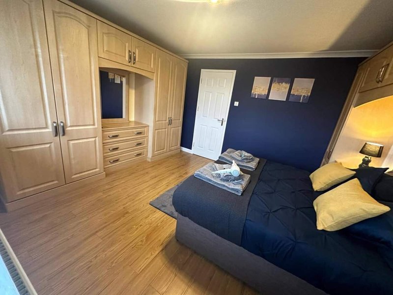 Spacious bedroom with double bed, built-in wardrobe, wooden flooring and navy accent wall