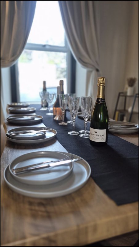 Formal dining table set with plates, glasses, champagne bottle and window view