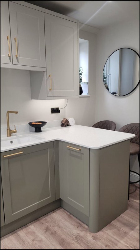 Modern kitchen with grey cabinetry, white countertop, brass hardware and circular mirror