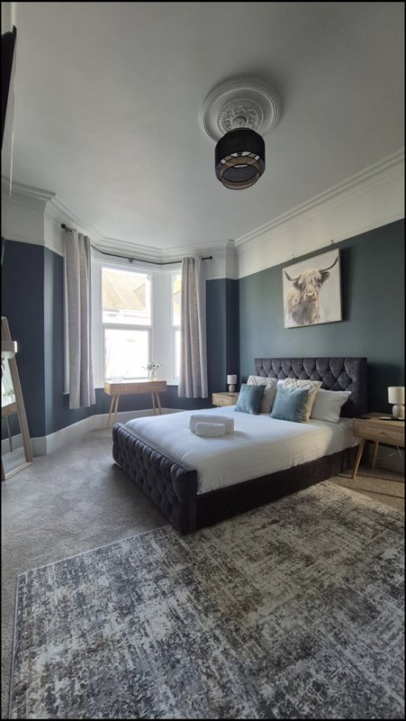 Modern bedroom with dark upholstered bed, blue accent wall, large window and contemporary furnishings
