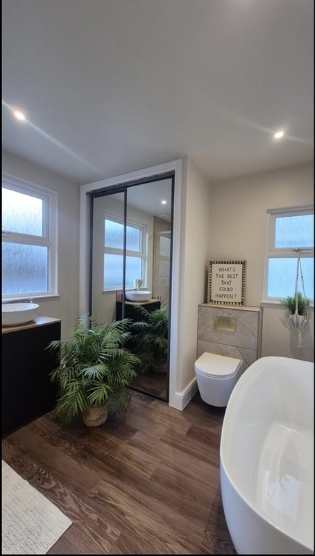 Modern bathroom with freestanding bathtub, toilet, plant, glass shower enclosure and windows