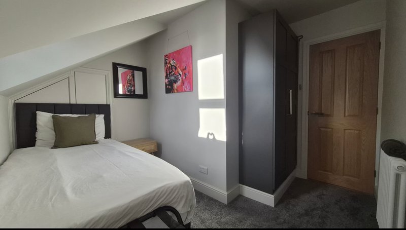 Bedroom with double bed, pink wall art, wooden door, and window with natural light