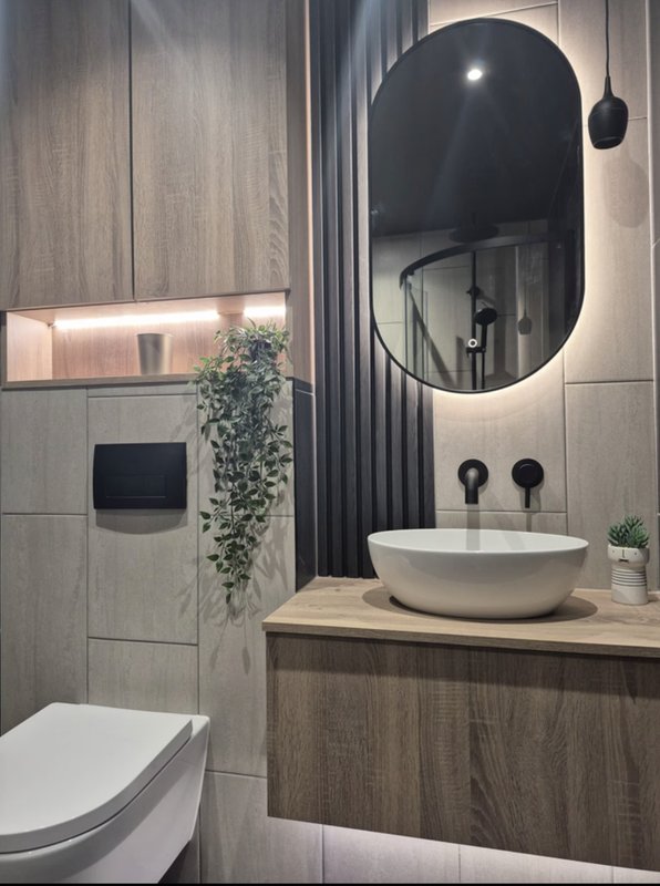 Modern bathroom with round mirror, vessel sink, wooden vanity and tiled walls