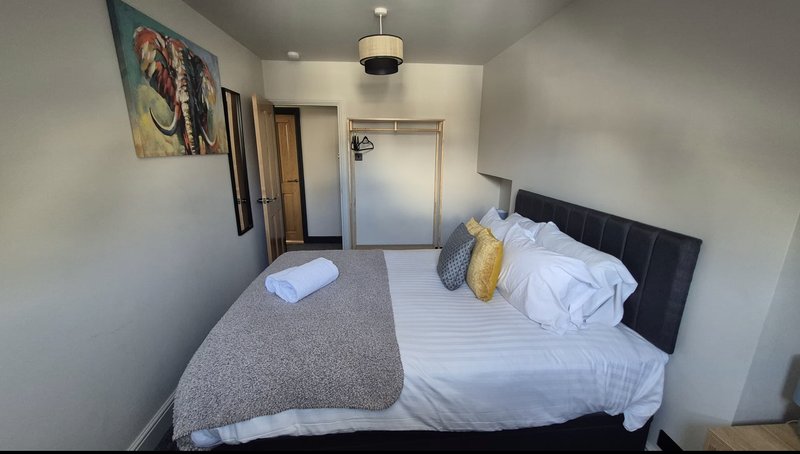 Bedroom with double bed, white bedding, grey throw, gold cushions and wall art