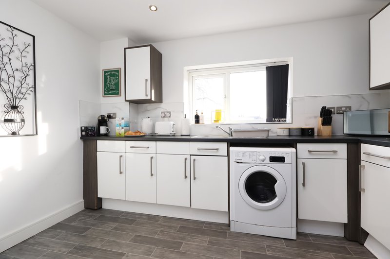 Modern kitchen with white cabinetry, black worktops, washing machine and window