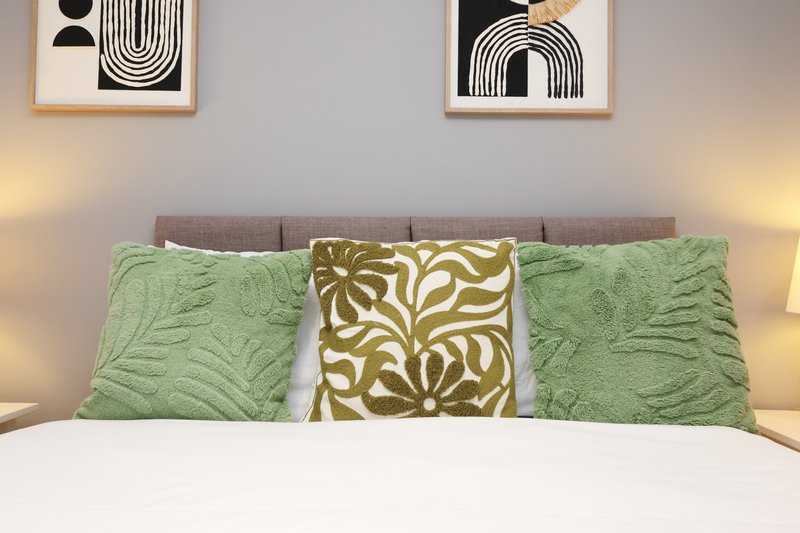 Bedroom with gray upholstered headboard, green quilted pillows, patterned cushion, and abstract wall art